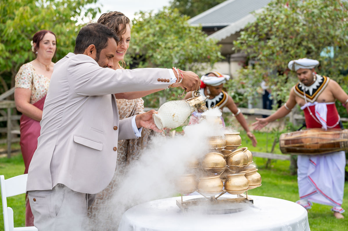 The bride and groom pouring milk into the gold pots as a drummer plays alongside
