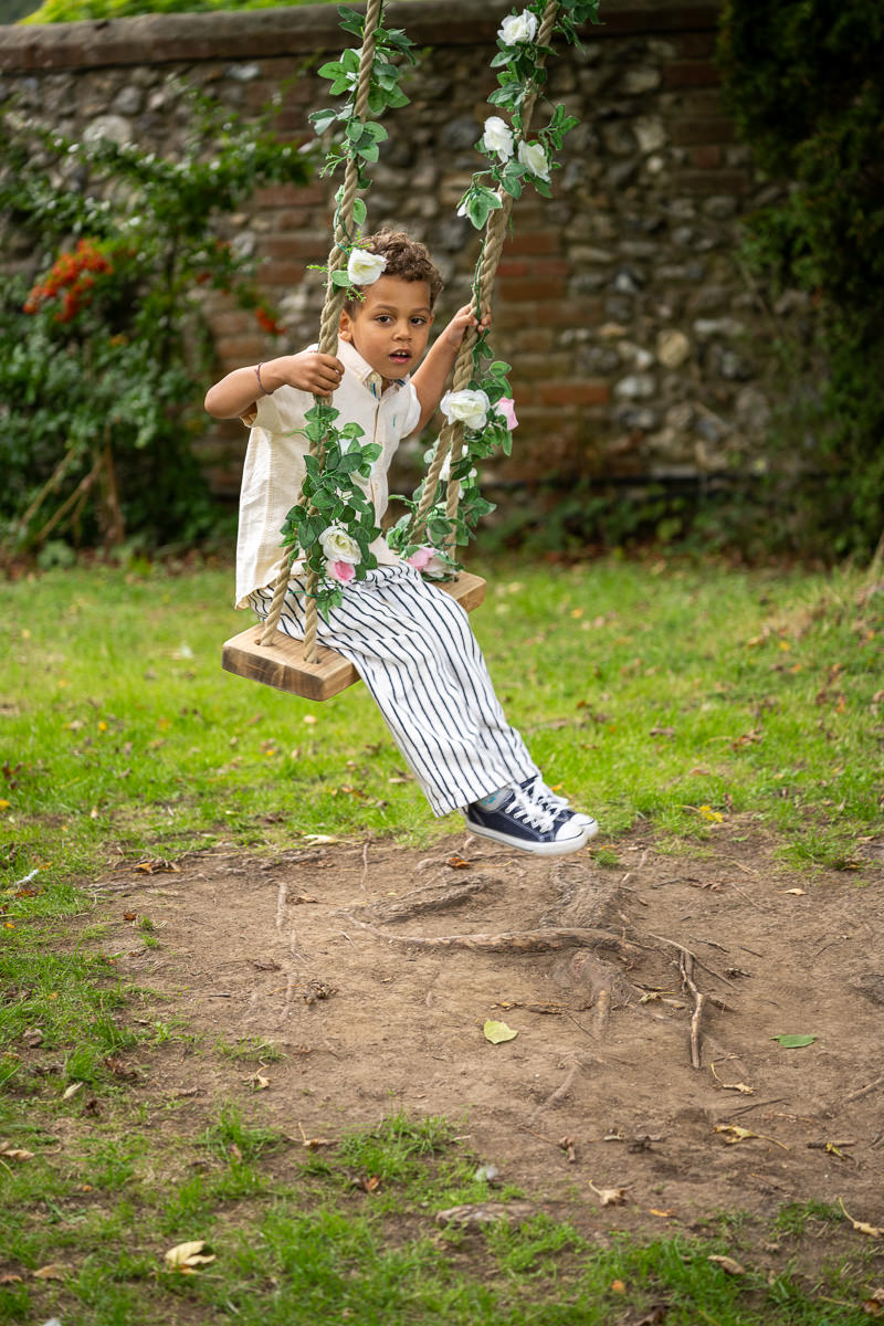 A page boy on the flower-covered swing in the garden at Selden Barns