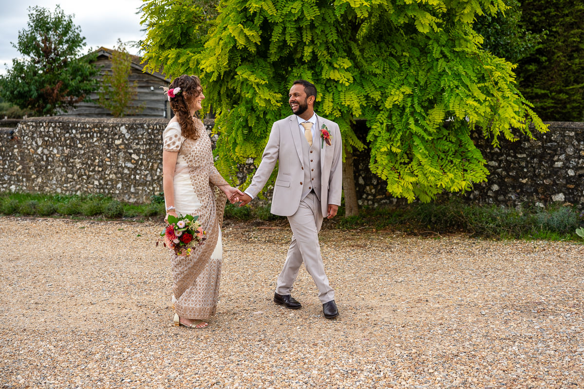 The bride and groom walking by the flint wall at Selden Barns
