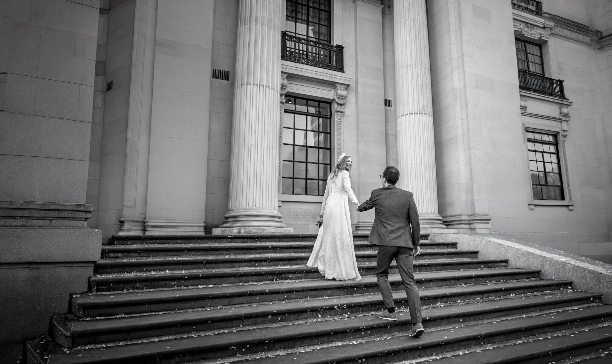 Bride smiling back at her groom as they climb the steps of Old Marylebone Town Hall, black and white