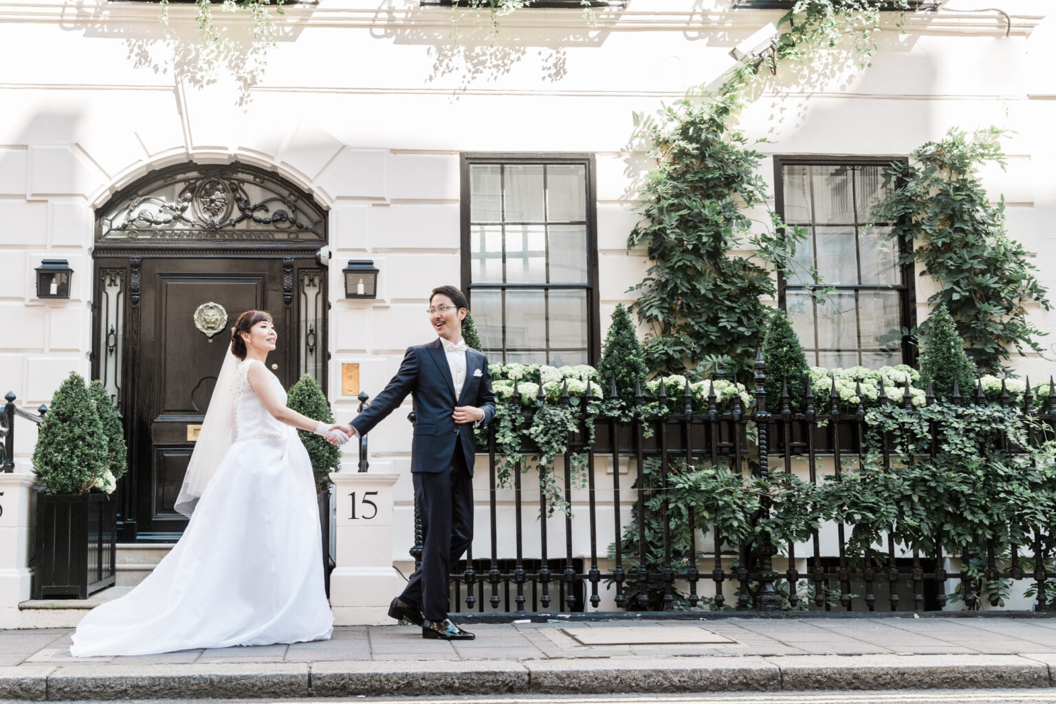 Bride and groom walking hand in hand past a white Georgian townhouse and ivy-covered railings in Mayfair