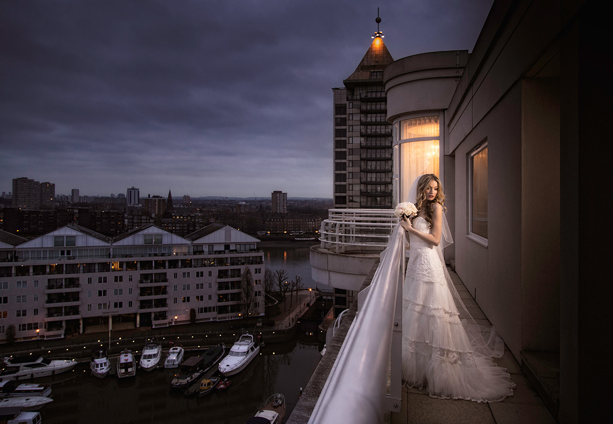 Bride on a hotel balcony at dusk with the city lights behind her