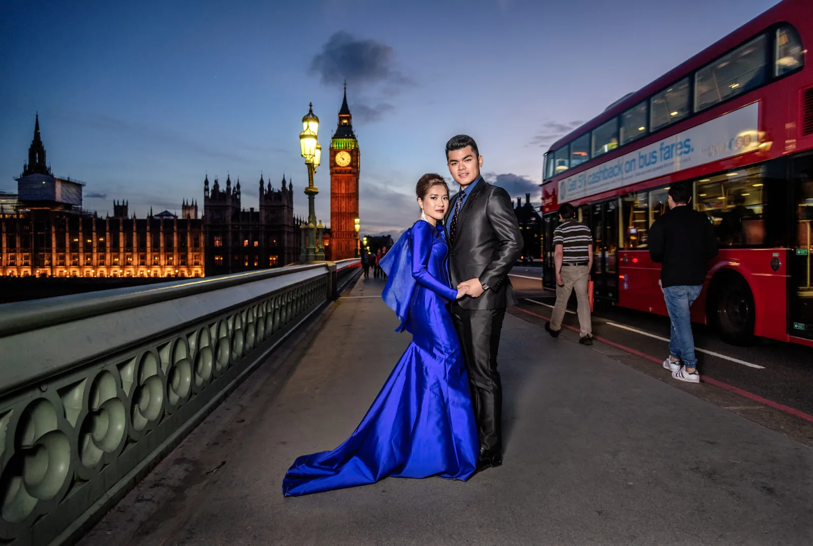 Bride in a royal blue gown and groom on Westminster Bridge at night with Big Ben and a red bus, London pre wedding shoot