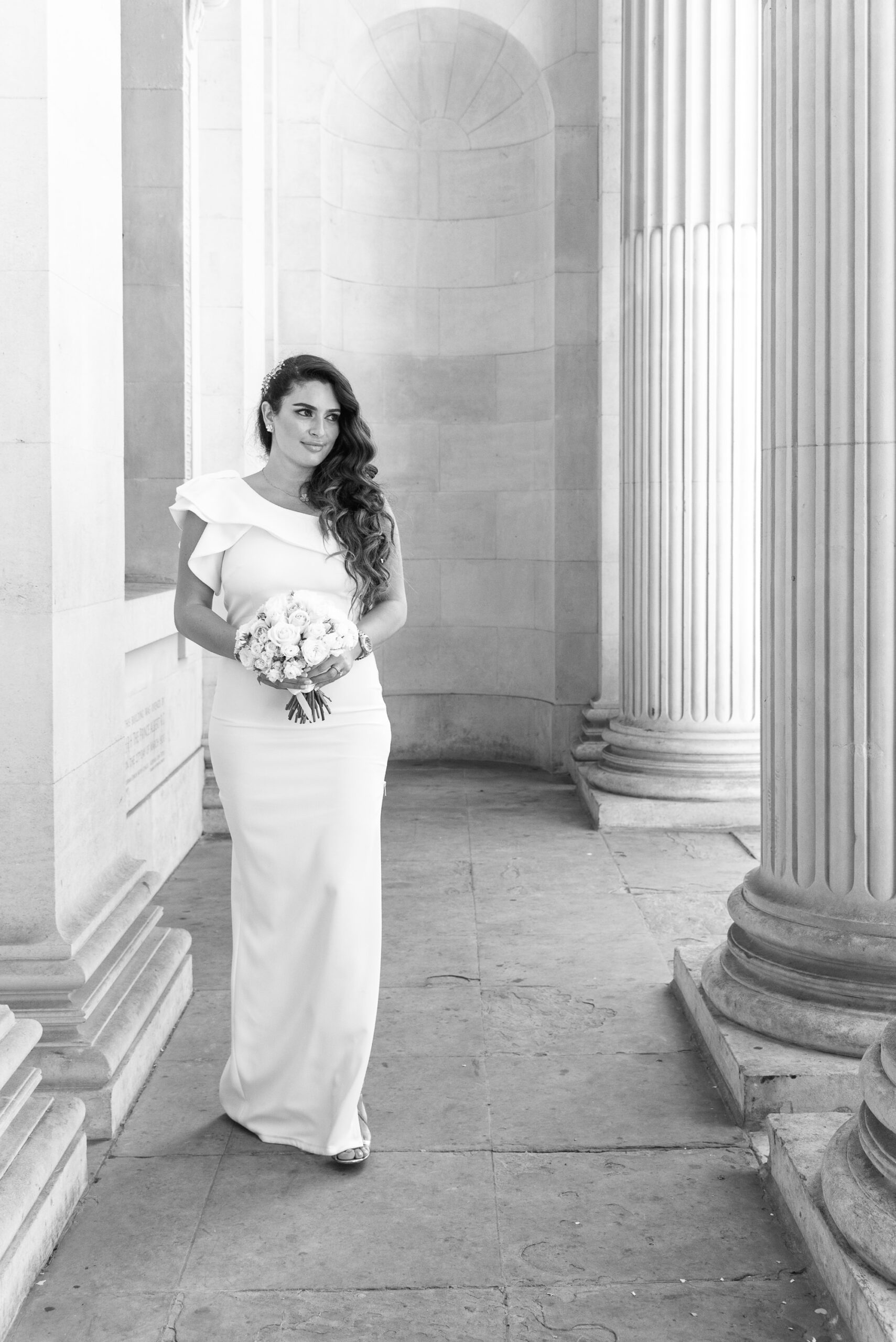 Black and white photo of Bibi in the colonnade at Old Marylebone Town Hall with her bouquet