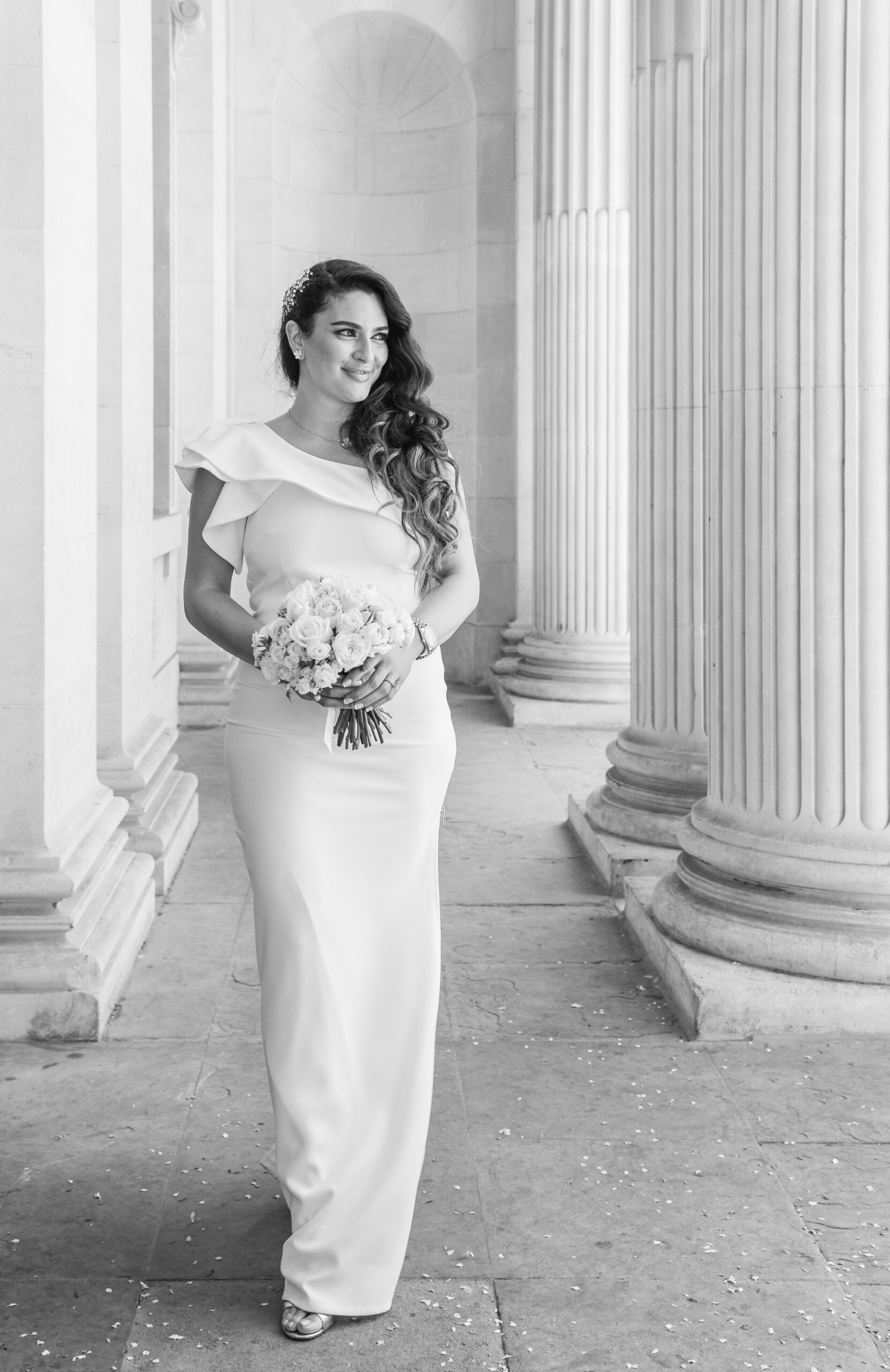 Black and white photo of Bibi walking between the columns at Old Marylebone Town Hall, looking over her shoulder