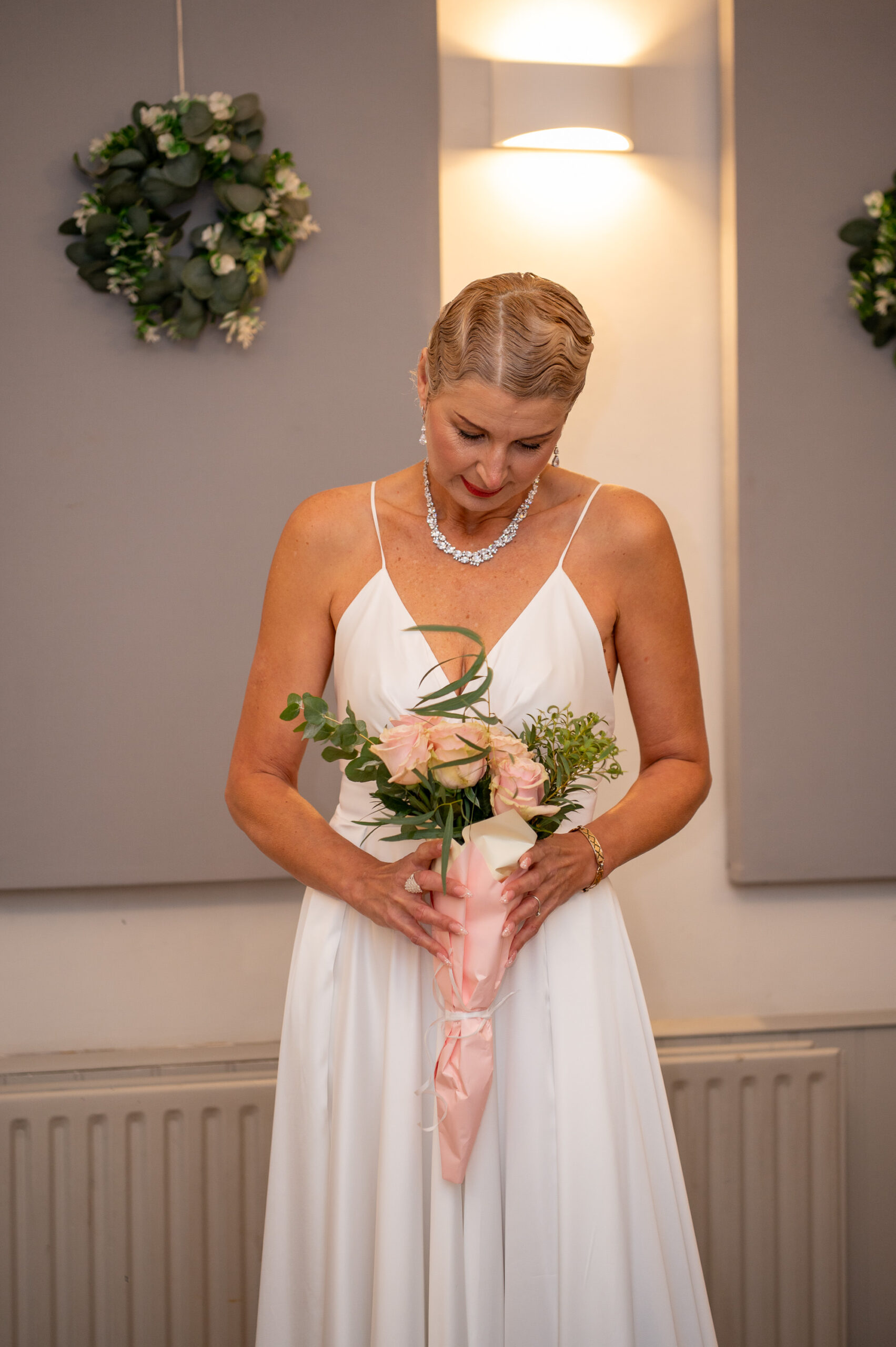 Nataliia in her white wedding dress looking down at her pink rose bouquet before the ceremony in Ealing