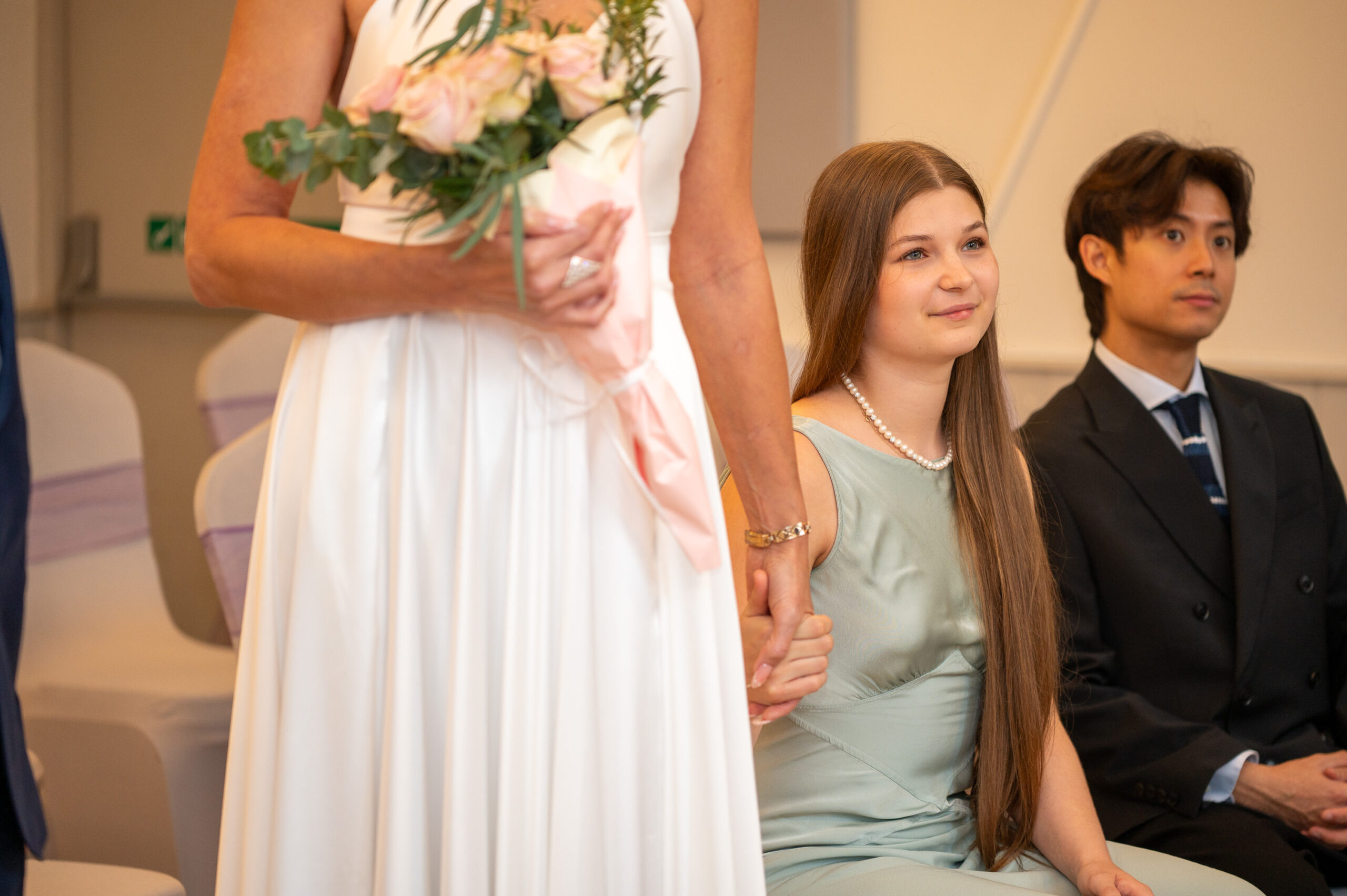 Nataliia holding her bouquet beside her daughter and a guest seated at the front of the ceremony room in Ealing