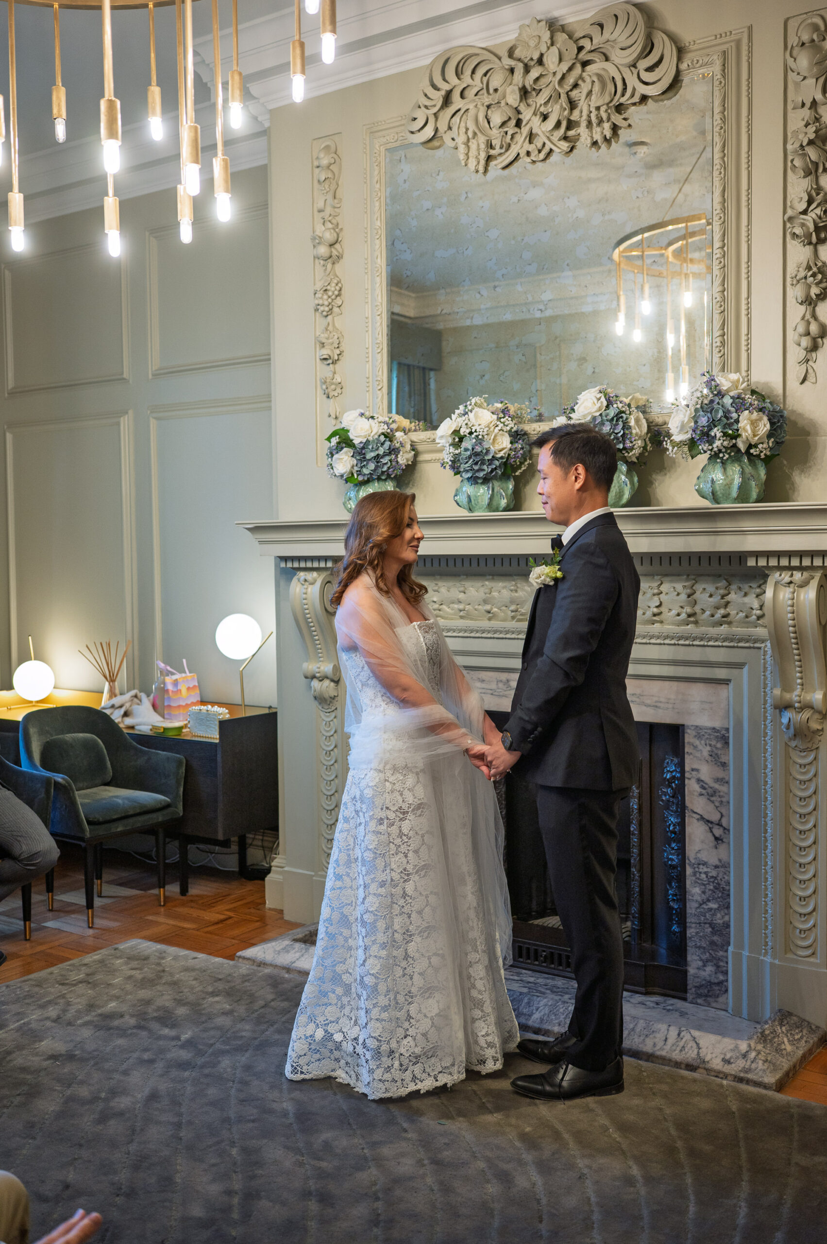 Nicoleta and Alistair holding hands in front of the fireplace during their ceremony in the Pimlico Room