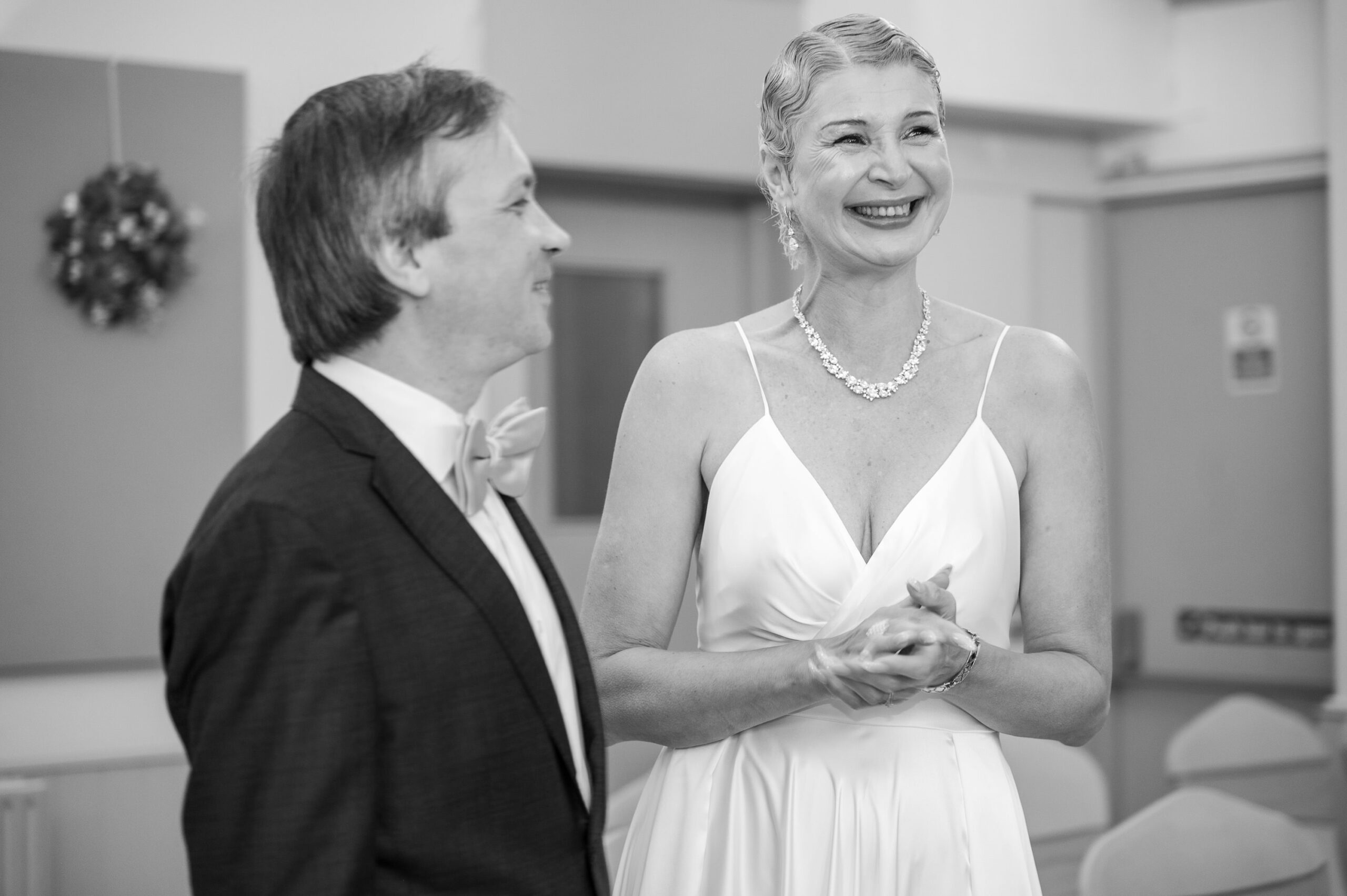 Black and white photo of Nataliia laughing as she faces Alexei during their Ealing wedding ceremony