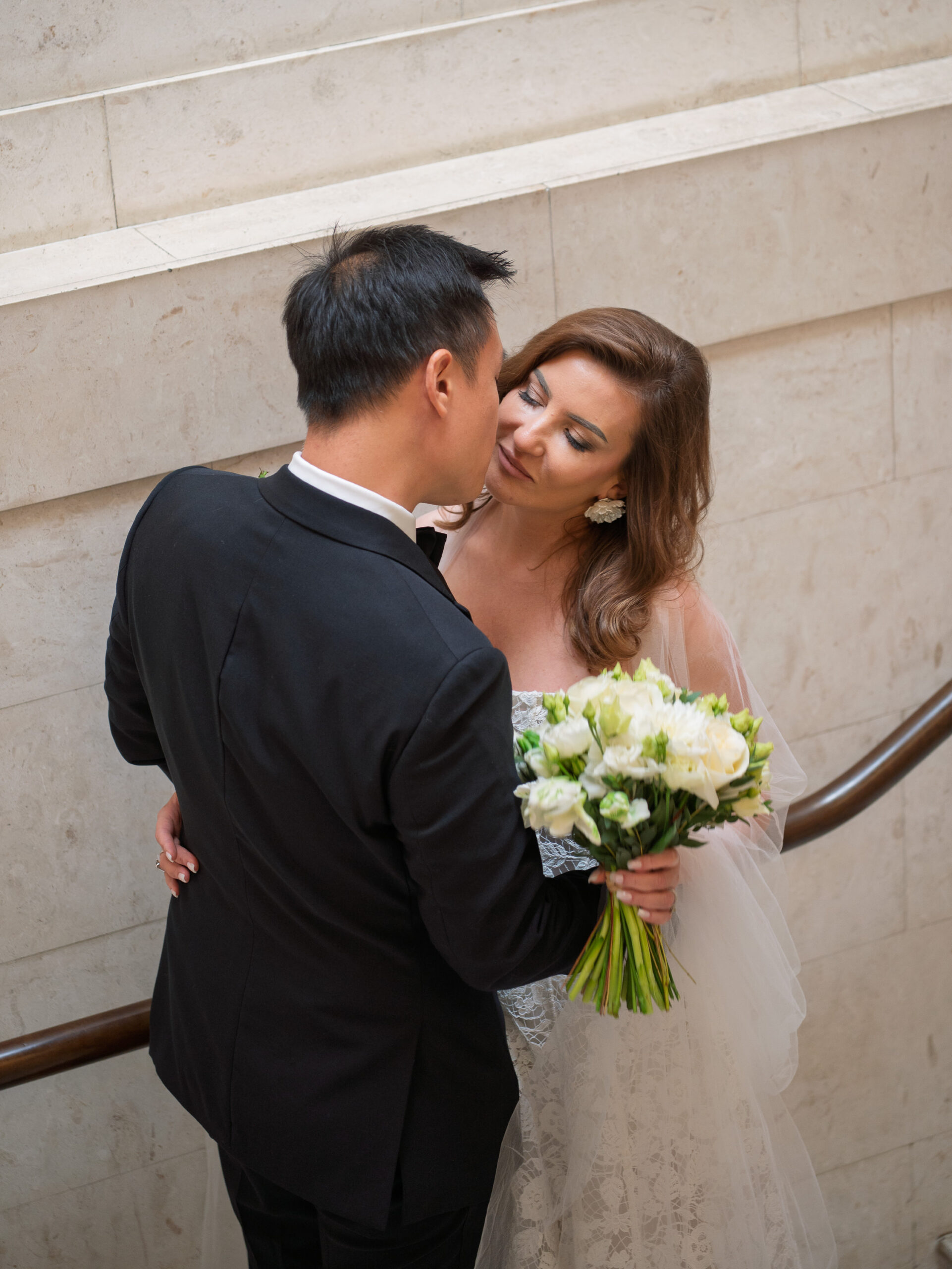 Alistair kissing Nicoleta on the cheek on the stone staircase at Old Marylebone Town Hall