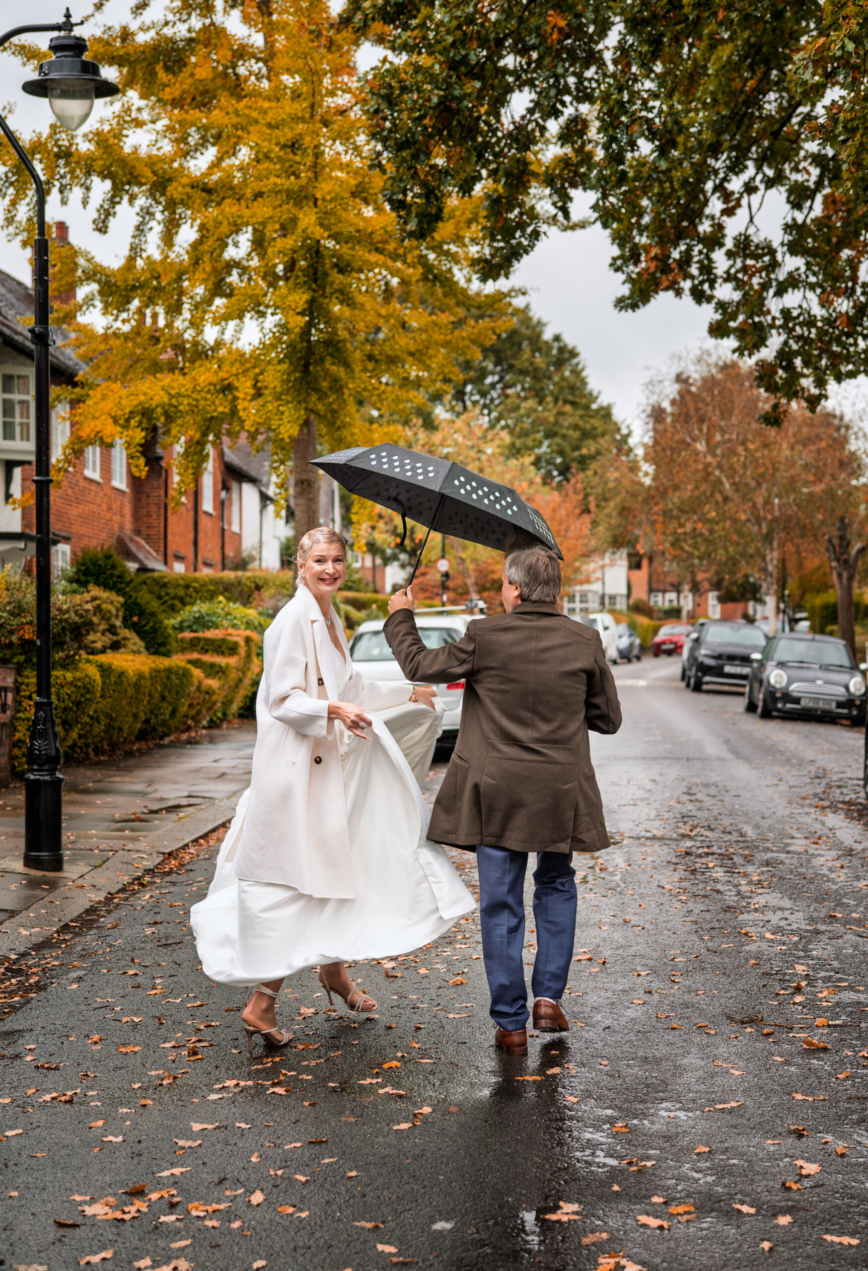 Nataliia twirling her dress under an umbrella with Alexei on a wet autumn street in Ealing, London