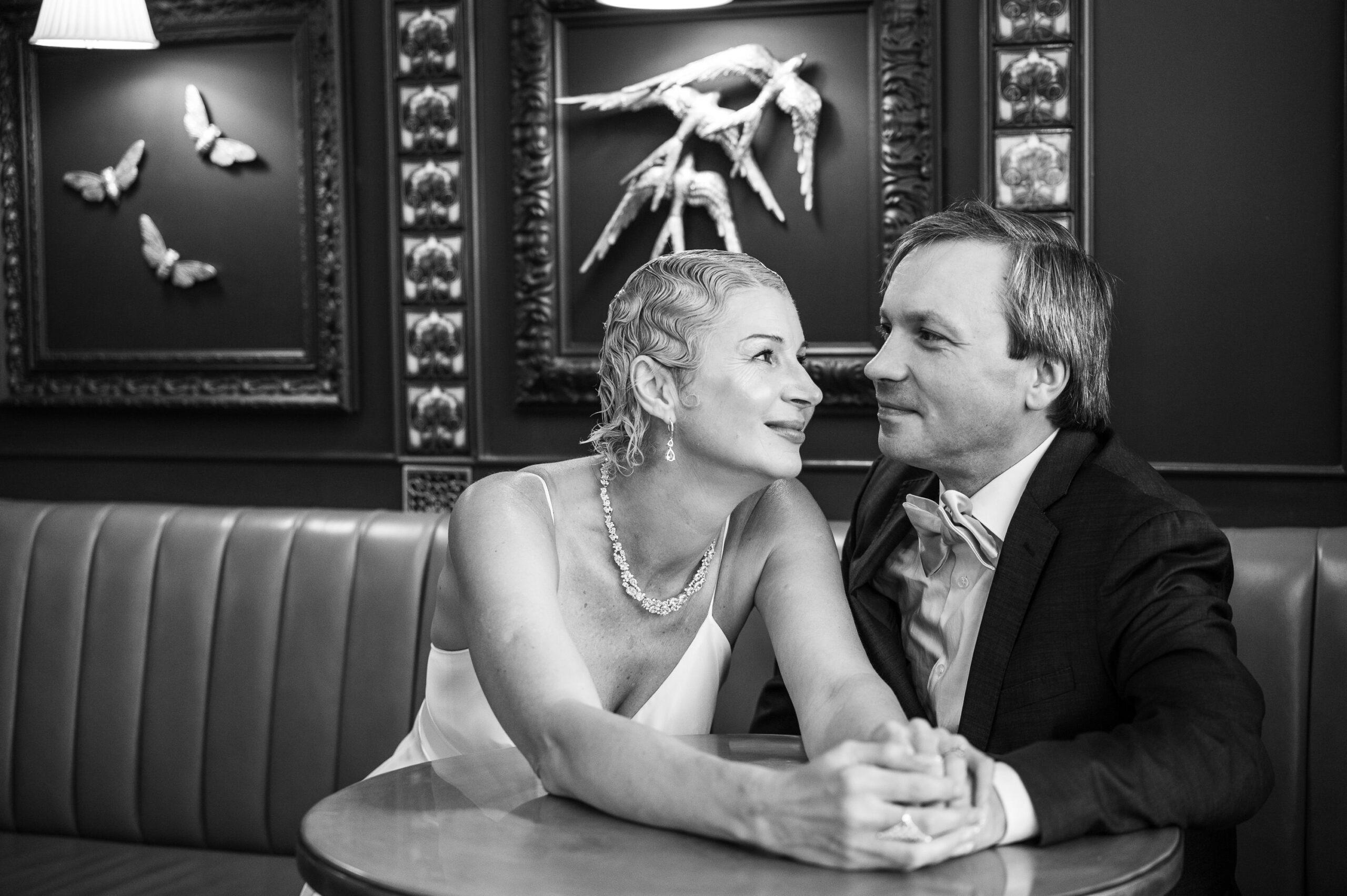 Black and white photo of Nataliia and Alexei holding hands at a table in The Village Inn, Ealing