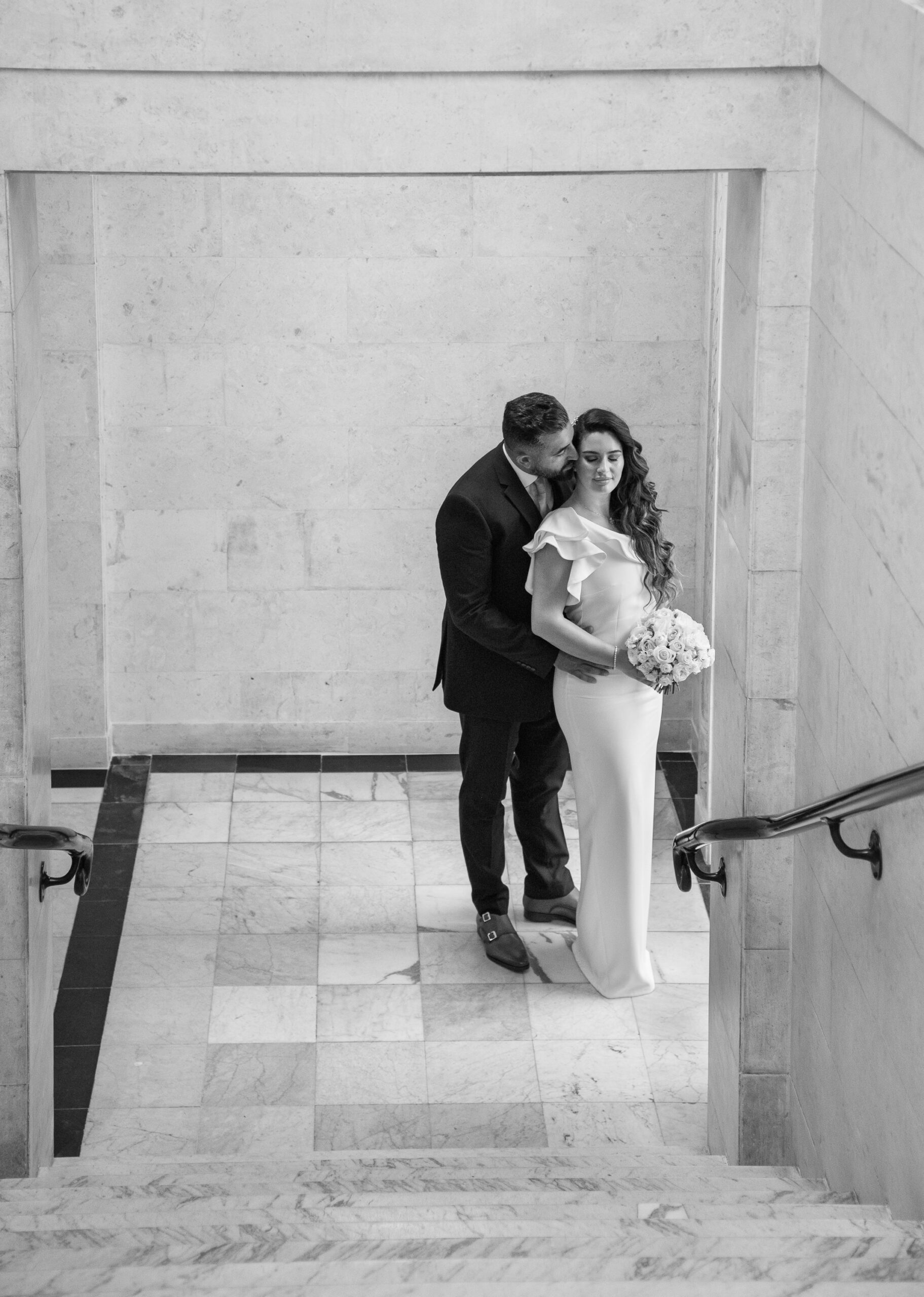 Black and white photo of Syrus kissing Bibi on the forehead on a marble landing at Old Marylebone Town Hall