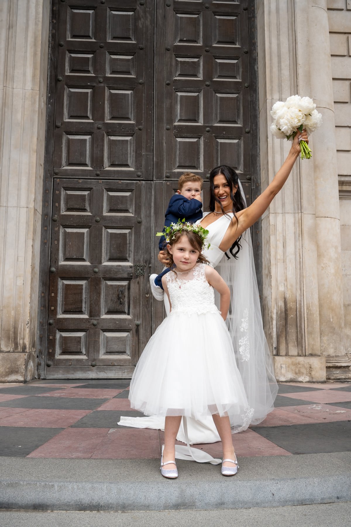 Sam laughing with her son and daughter at the west doors of St Paul's Cathedral, bouquet raised in the air