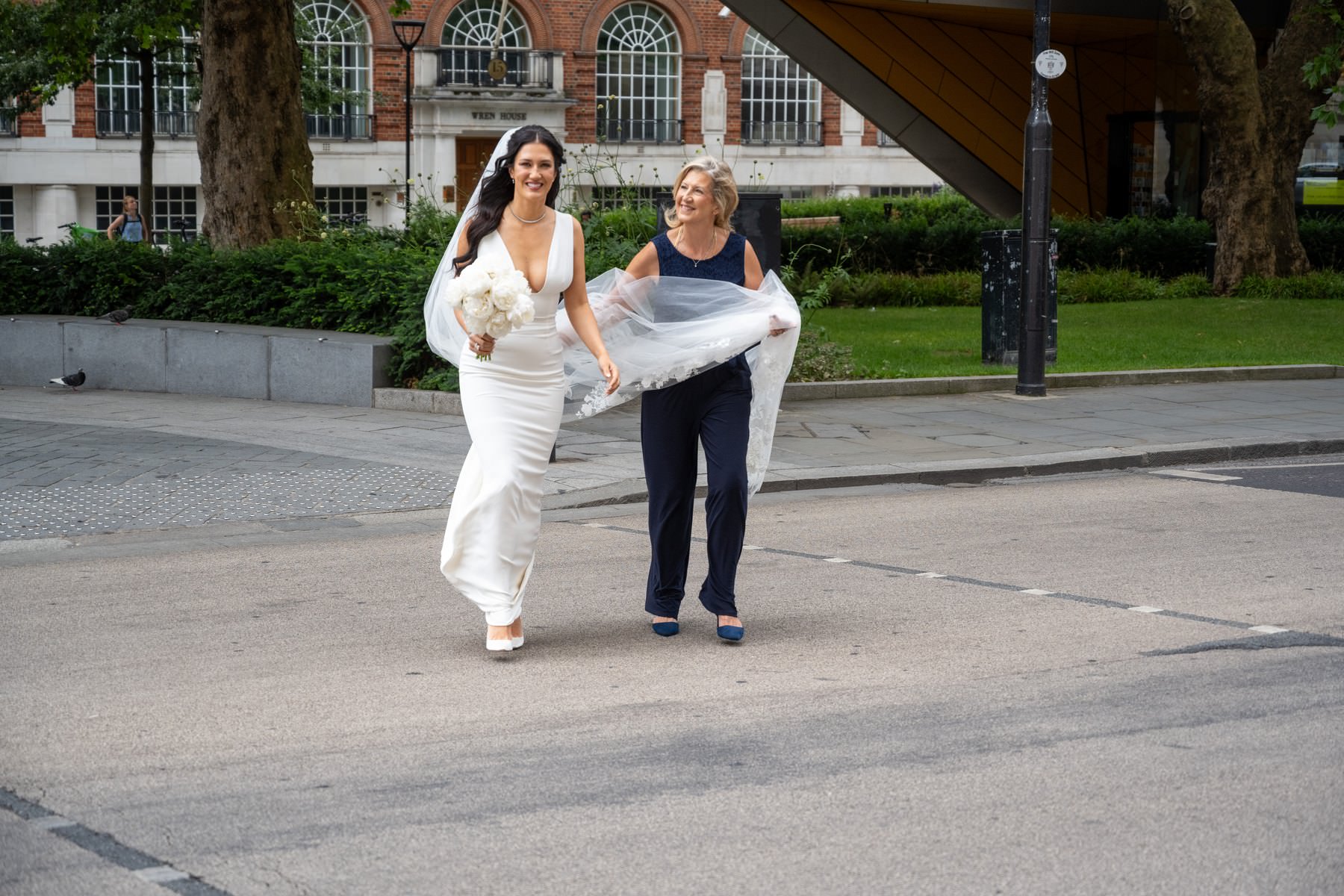 Sam and her mum crossing the road with the veil held up and a red London bus behind them