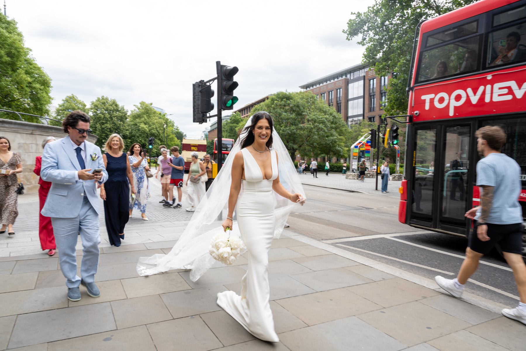 Sam crossing the street near St Paul's Cathedral with her veil flying behind her and a red bus beside her