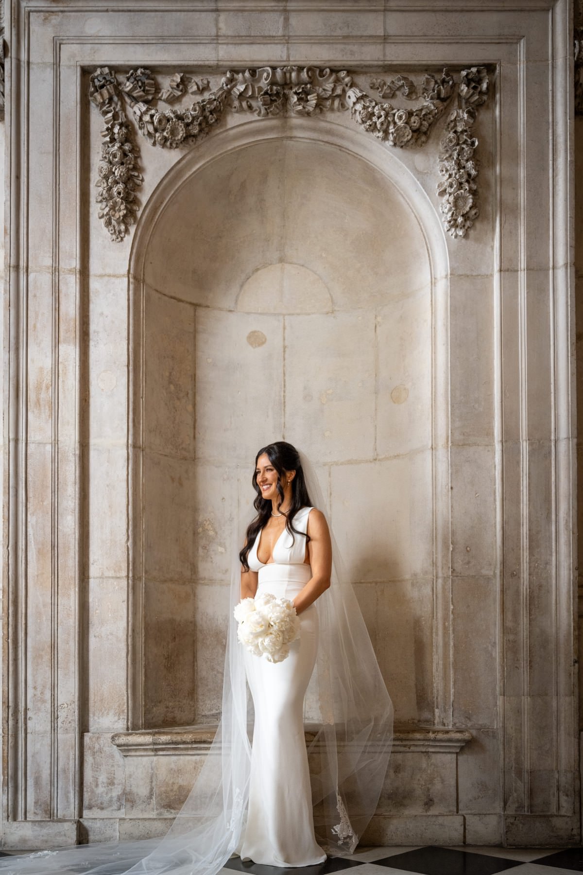 Sam standing in a carved stone niche inside St Paul's Cathedral holding her bouquet