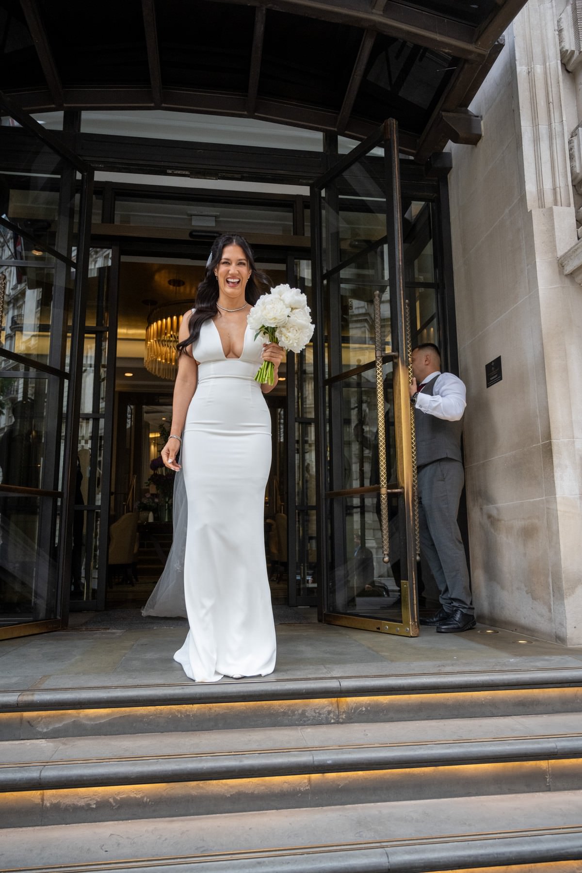 Sam in her wedding dress stepping out through the revolving doors of the Corinthia hotel on Whitehall