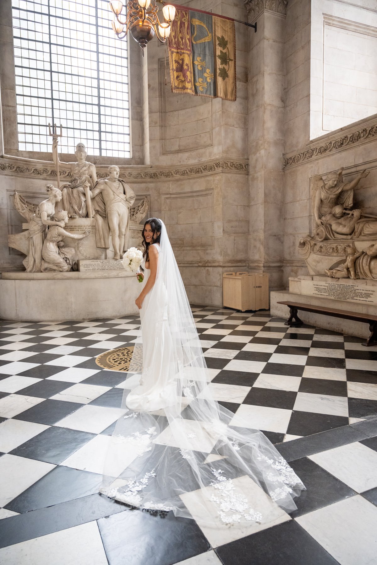 Sam's long veil spread across the black and white marble floor in front of a statue inside St Paul's Cathedral