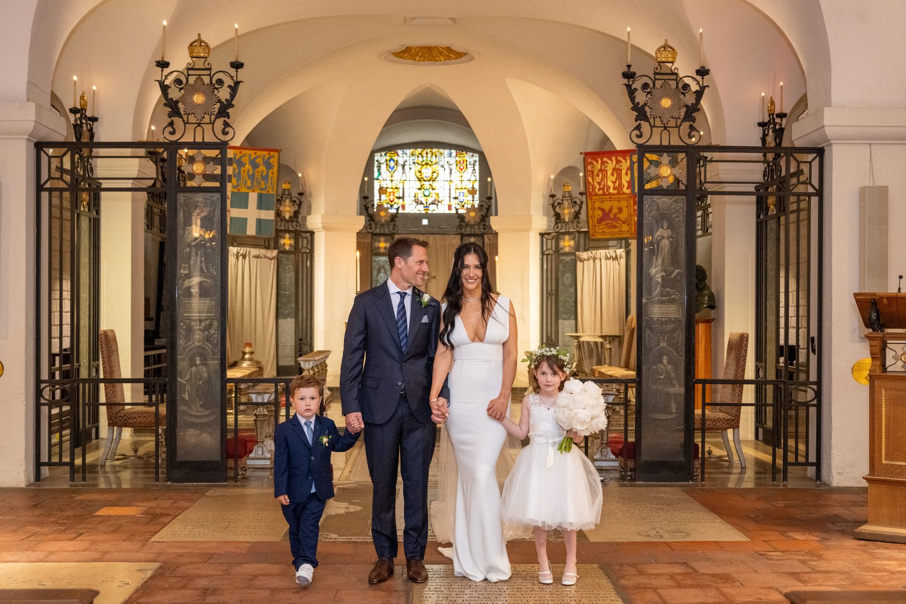 Sam and Matt walking out of the OBE Chapel with their son and daughter holding their hands