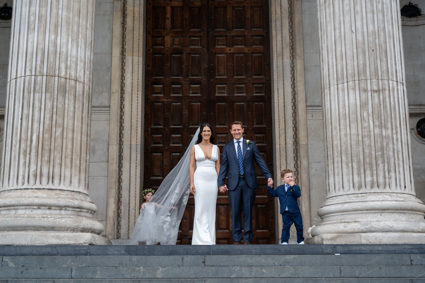 Sam and Matt on the steps of St Paul's Cathedral with their children, Sam's veil caught in the breeze