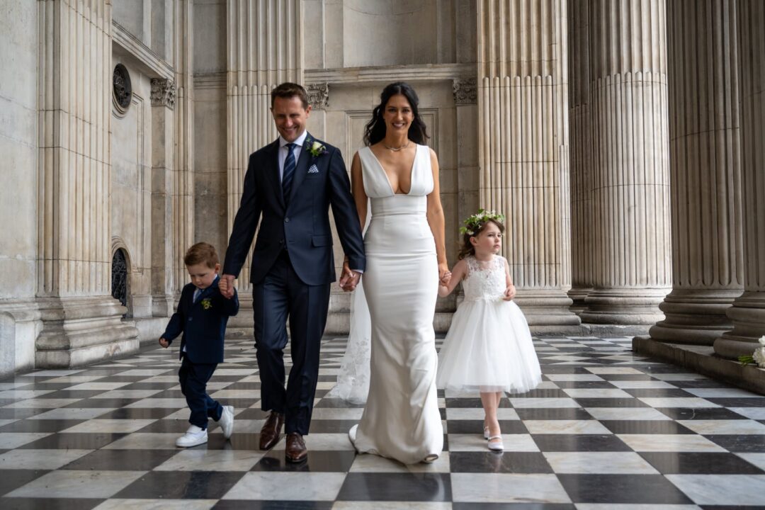 Sam and Matt walking hand in hand with their two children across the chequered floor of the portico at St Paul's Cathedral