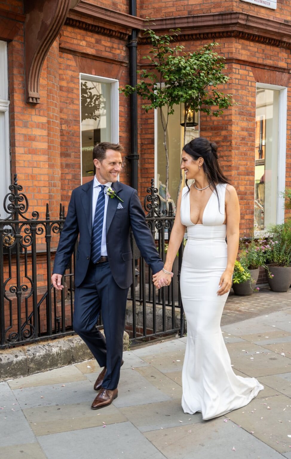 Sam and Matt walking past red brick and black railings in Mayfair after their wedding