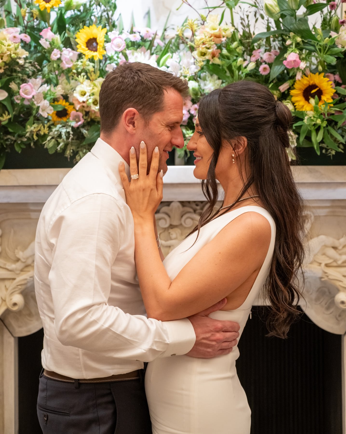 Sam and Matt holding each other in front of a flower arrangement with sunflowers at Bacchanalia