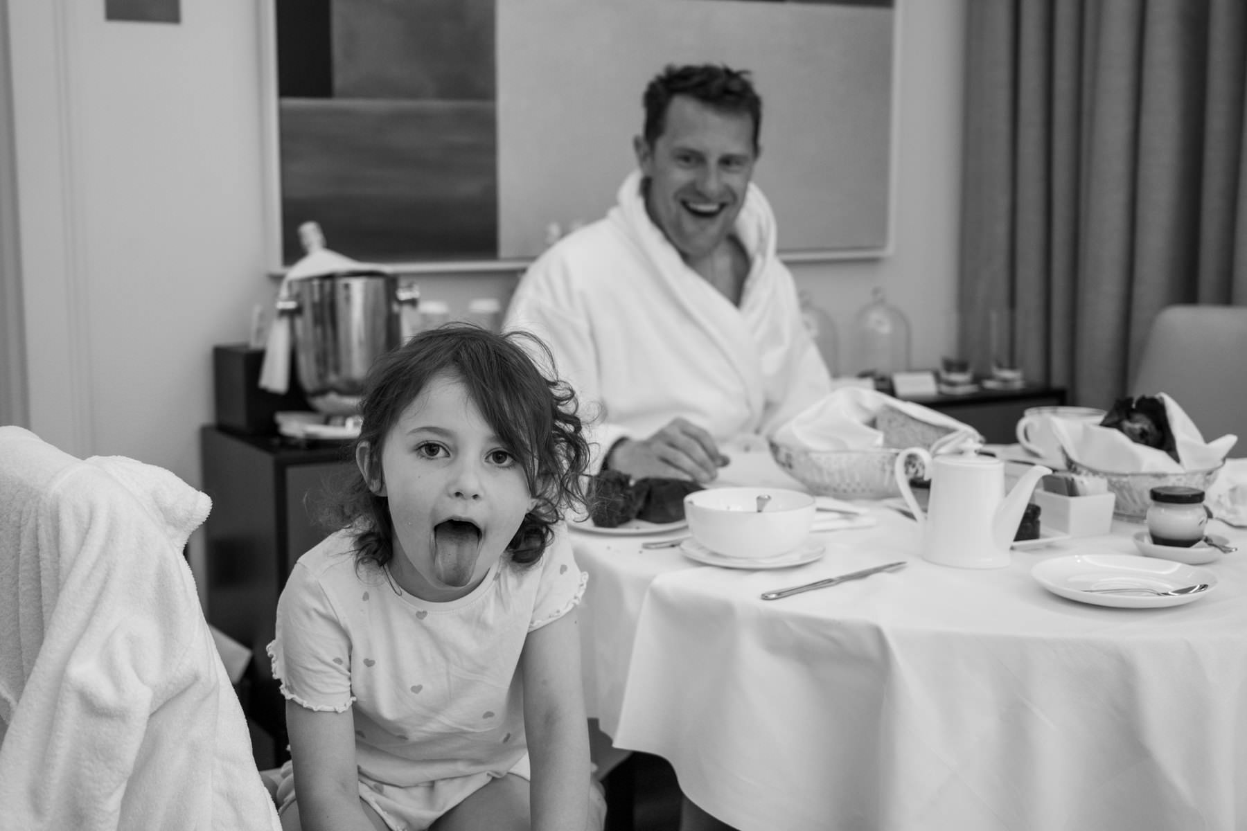 Black and white photo of Matt in his dressing gown at the breakfast table with his daughter pulling a face